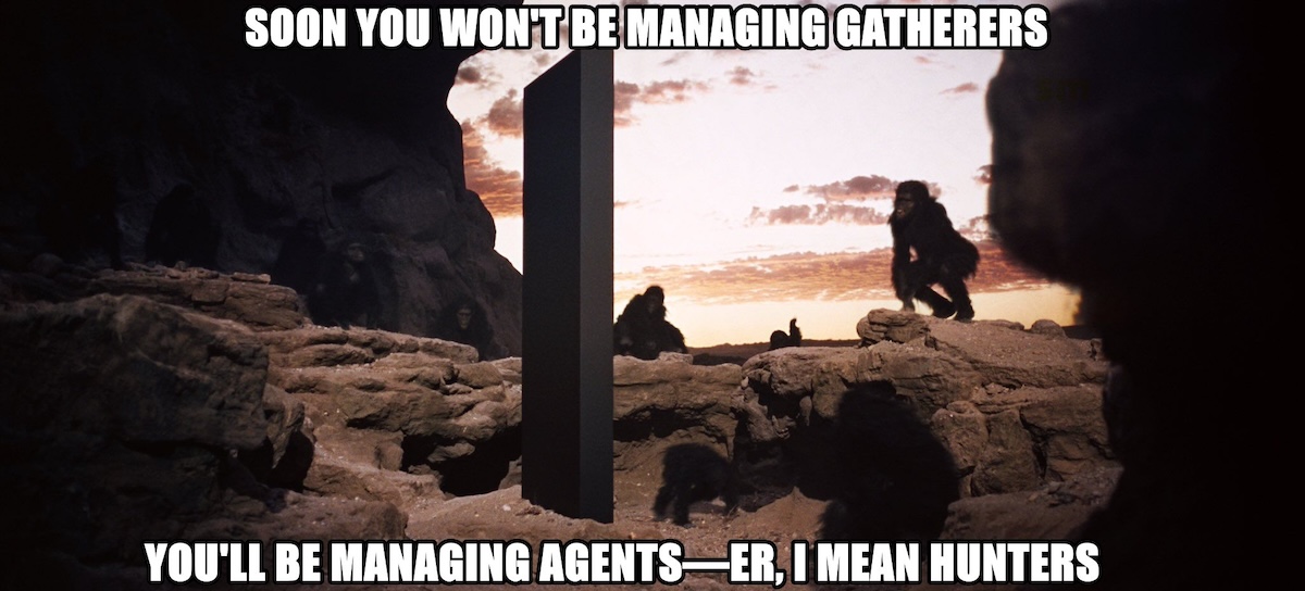 A meme-style image inspired by 2001: A Space Odyssey: a group of early hominids stand and crouch among rocky terrain at sunrise, surrounding a tall black monolith in the center. Overlaid white Impact-style text reads at the top, "SOON YOU WON’T BE MANAGING GATHERERS,"" and at the bottom, "YOU'LL BE MANAGING AGENTS—ER, I MEAN HUNTERS,"" humorously comparing modern AI agent hype to prehistoric evolution.
