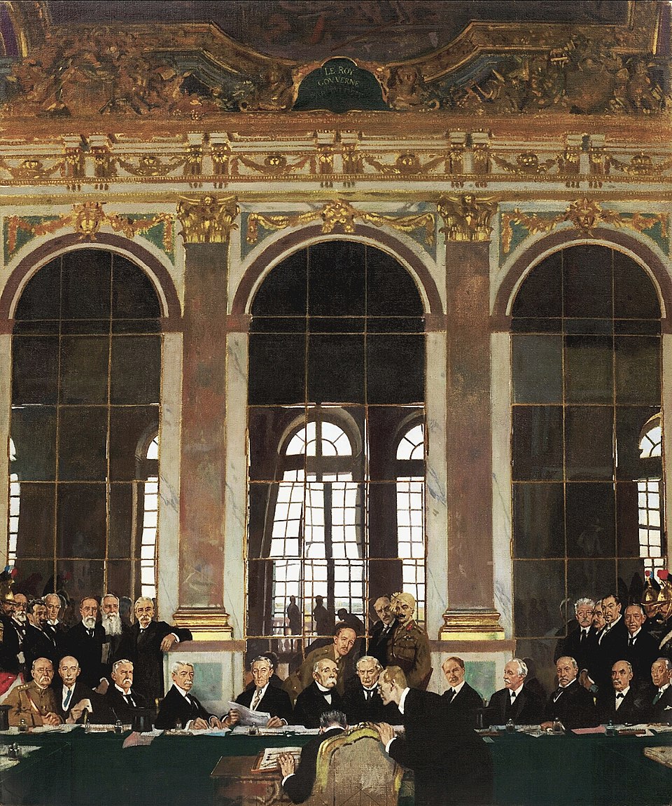 Delegates seated at a long table in the Hall of Mirrors at Versailles, signing the Treaty of Versailles in 1919, with tall arched mirrors and ornate chandeliers reflected behind them.