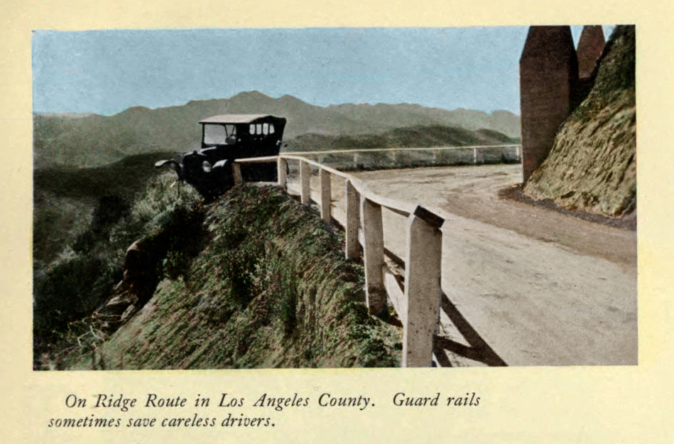 A colorized 1920s postcard photograph of an automobile perched on a narrow ridge road in Los Angeles County, with a wooden guardrail along the precipitous edge; a caption at the bottom reads "Guard rails sometimes save careless drivers."